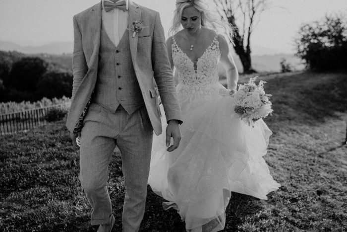 Brautpaar geht Hand in Hand über eine Wiese in Schwarzweiß – Hochzeitsfotografie in Kärnten von Mathias Taxer